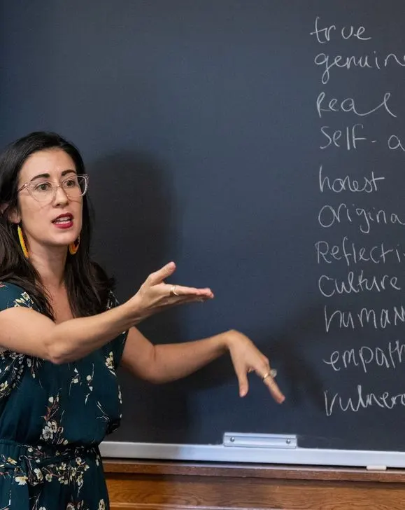 professor motioning calling on a student while standing in front of a blackboard